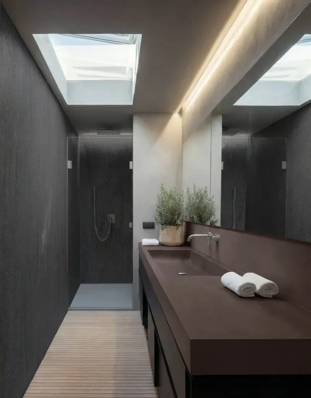 Wąska łazienka z ciemnym blatem Corian® z umywalką zintegrowaną i ścianami z tego samego materiału