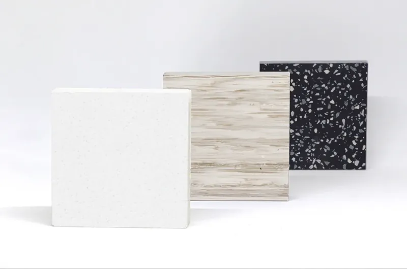 Trzy próbki płyt solid surface: biała, w dekorze drewna i czarna z drobinami